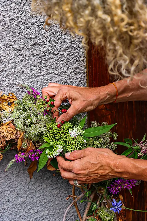 Deux mains composent un bouquet de fleurs sauvages contre un mur crépi